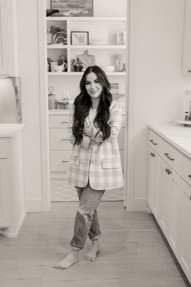 Britllin Noe descalza en una cocina, con los brazos cruzados, sonriendo